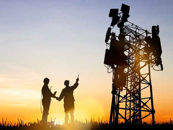Engineers silhouetted against sunset near telecommunication cell tower