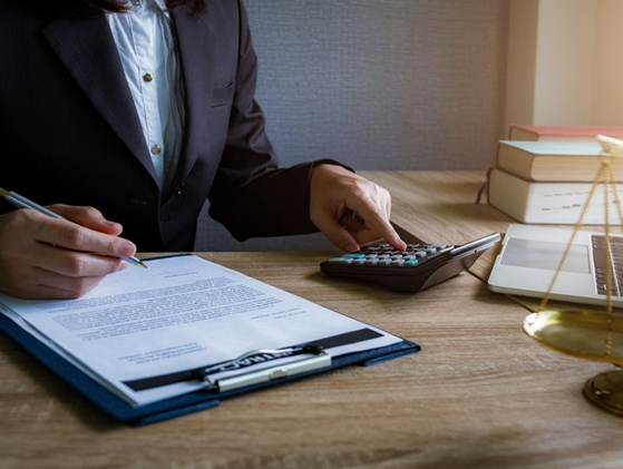 Professional filling out legal and compliance documents at desk with calculator and scales of justice