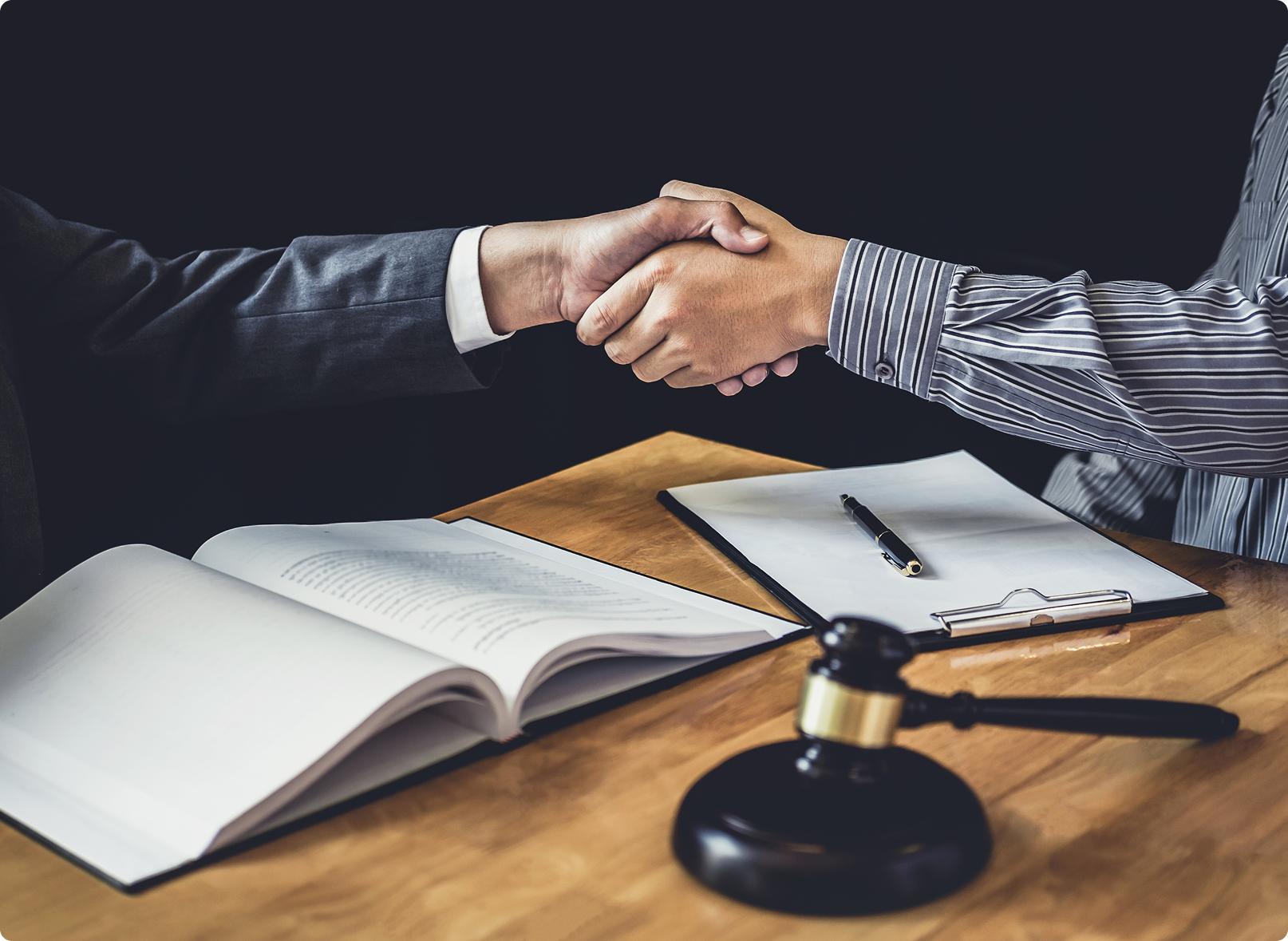 Two businessmen shaking hands over a desk with a legal gavel